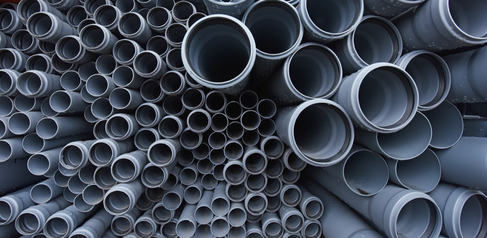 Gray PVC pipes with bell ends stacked at a pipe plant