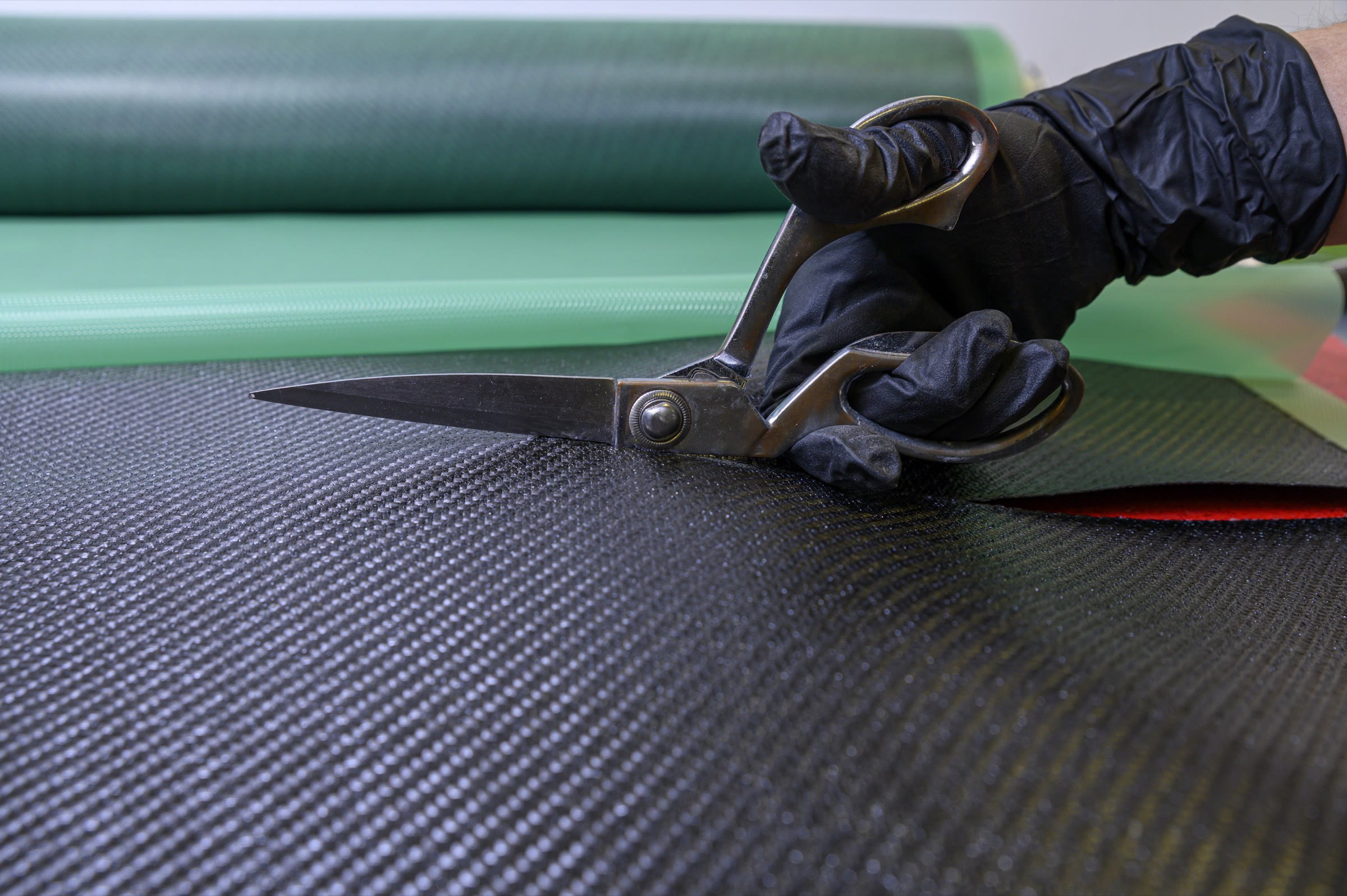 Gloved hand cutting a carbon fiber sheet with shears on a workbench