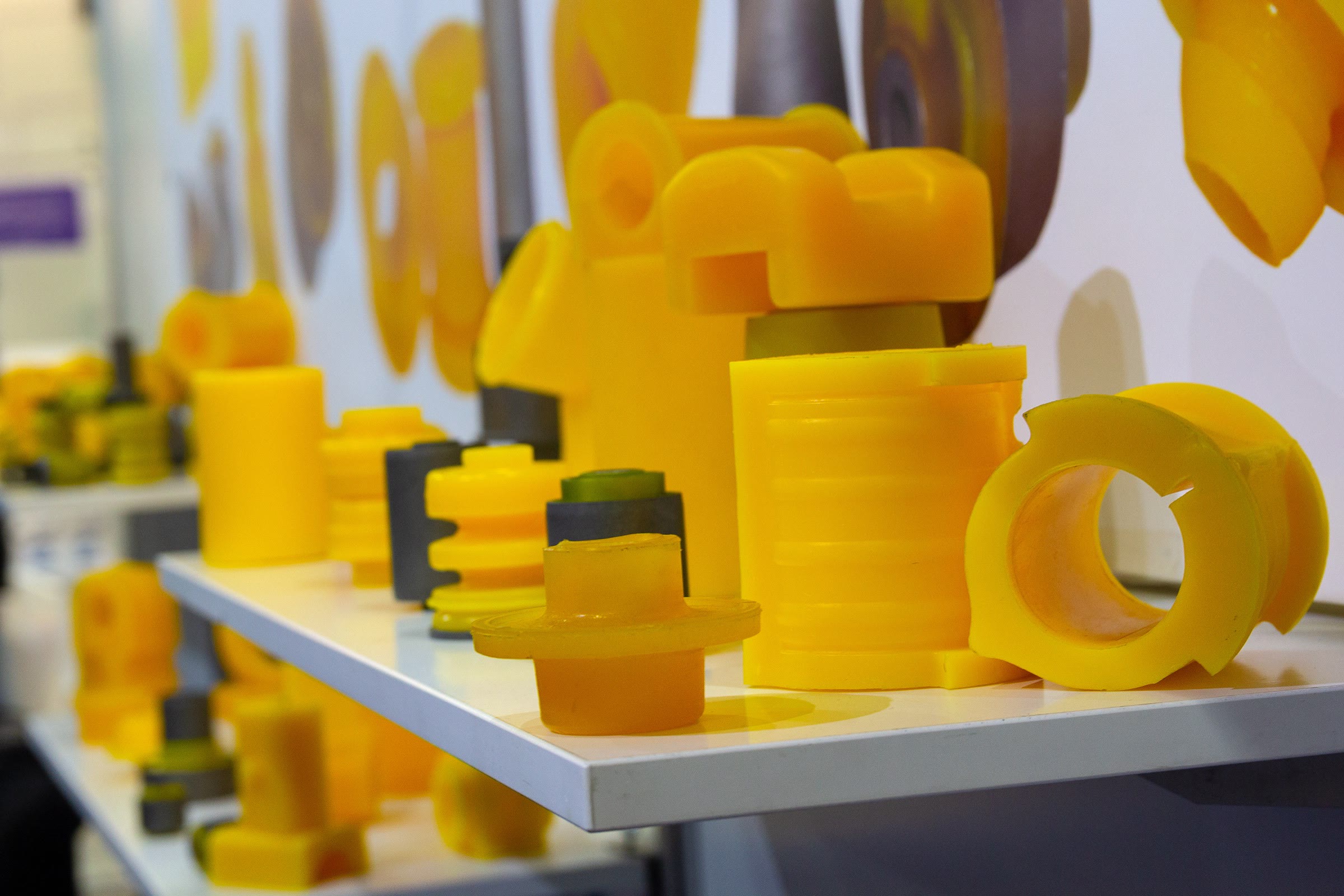 Yellow cast polyurethane machine parts, bushings and rollers displayed on a white shelf