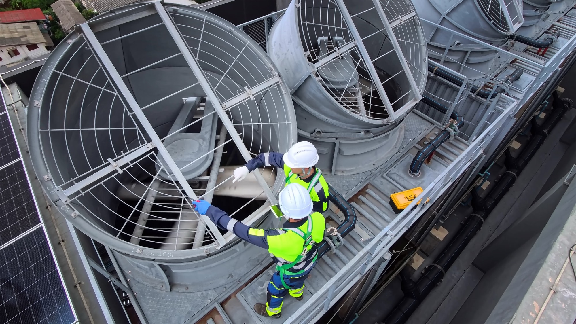 Two technicians in safety gear inspecting rooftop cooling tower fans