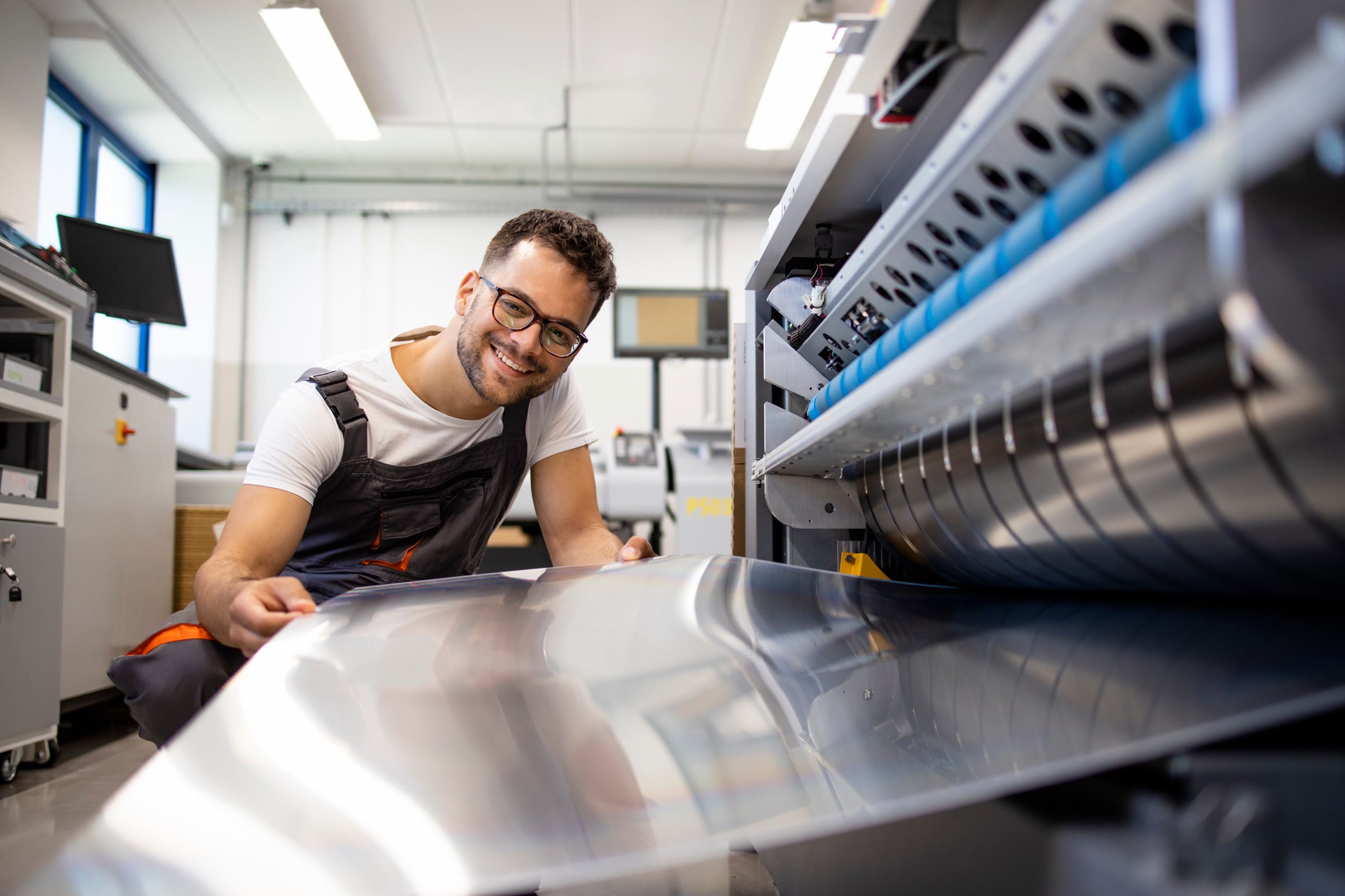 A print worker feeding a large aluminum printing plate into a plate machine