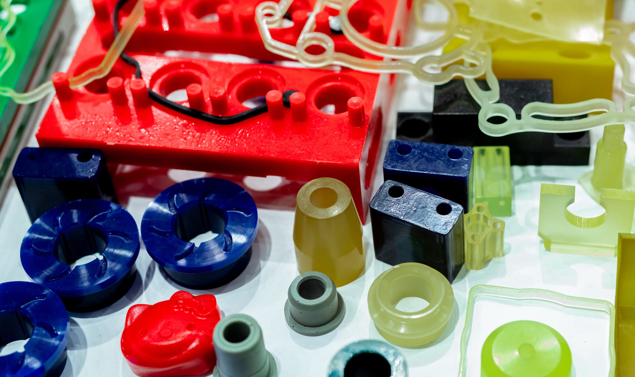 Cast polyurethane parts in blue, red, black, amber, and green laid out on a bench, each colored through the full cross-section