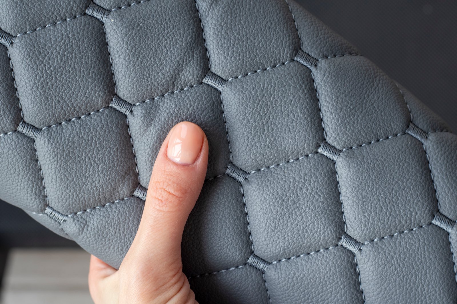 A hand pressing on a quilted grey synthetic leather panel