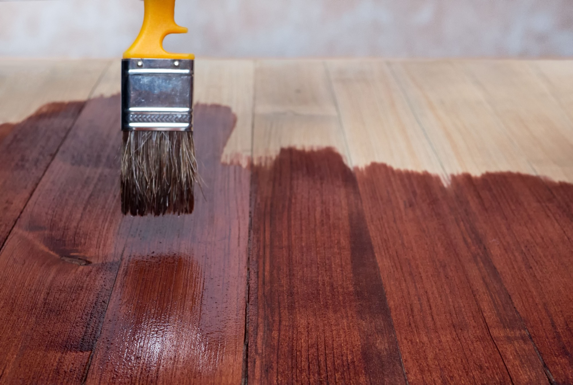 Brush applying amber shellac finish to a wood floor, finished and bare wood side by side