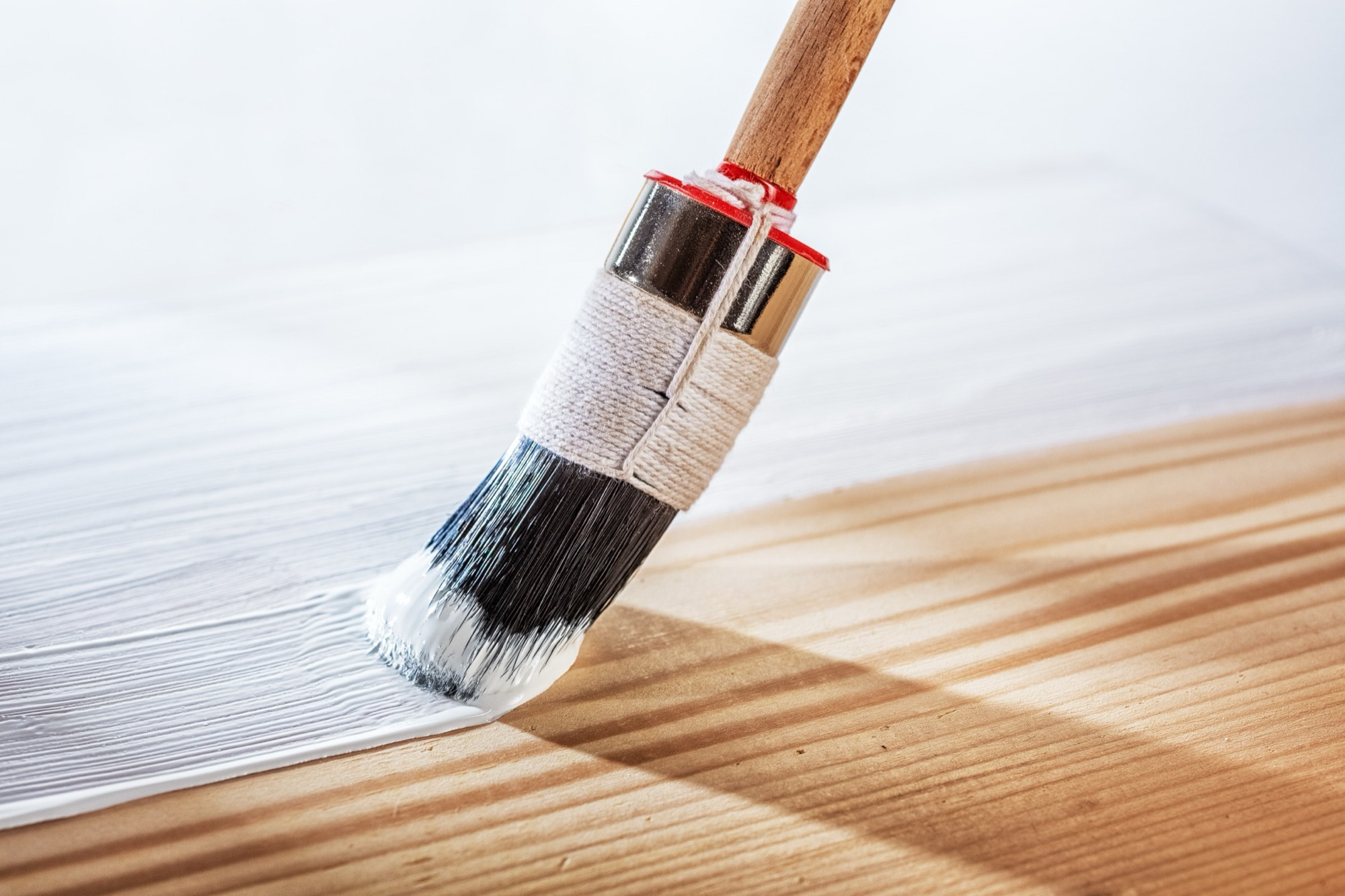 Brush applying white primer to bare wood