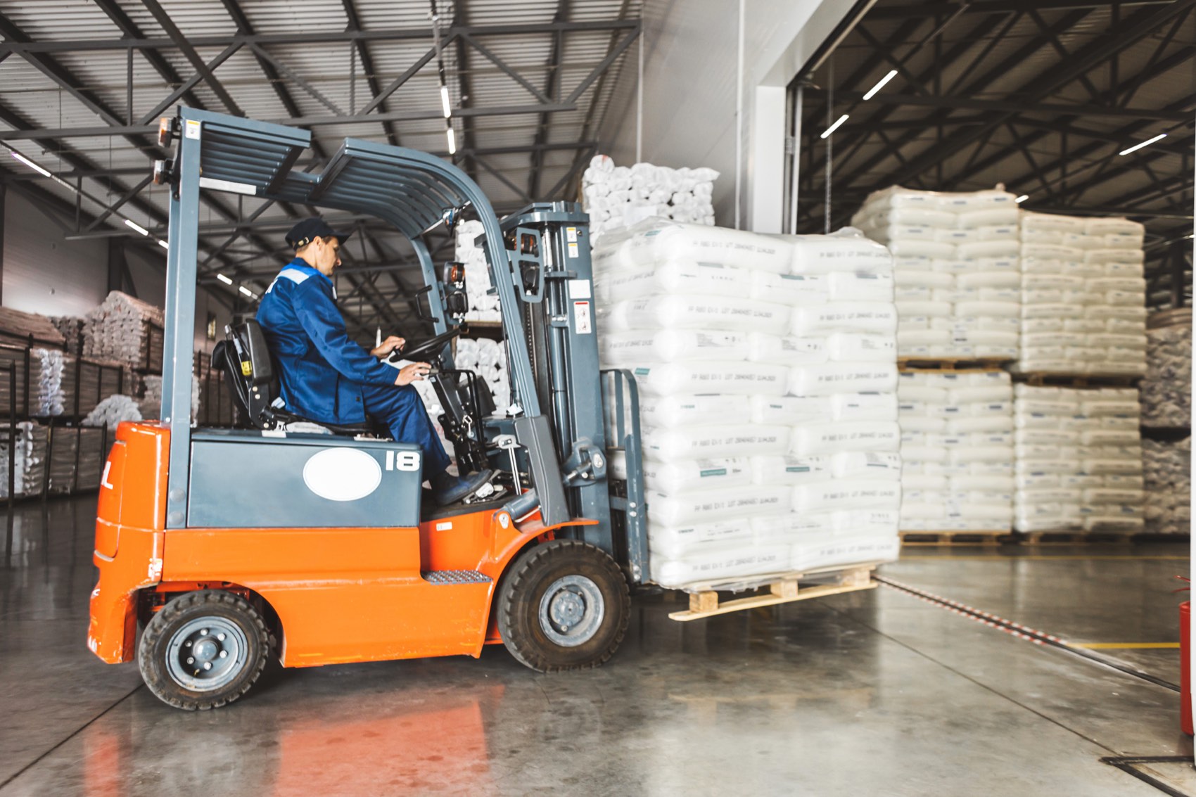 Forklift moving a wrapped pallet of raw material bags in a warehouse