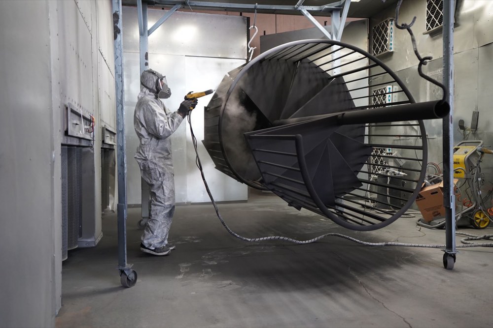 Technician spray-coating a fabricated metal part in an industrial finishing booth
